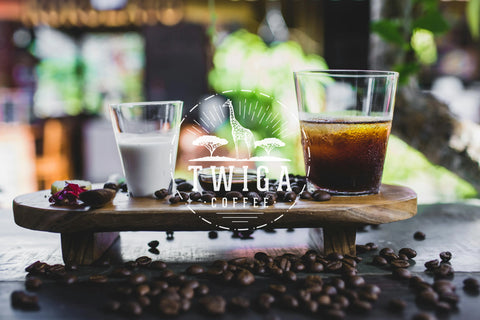 A glass of milk and a glass of cold brew coffee on a wooden board, surrounded by coffee beans.