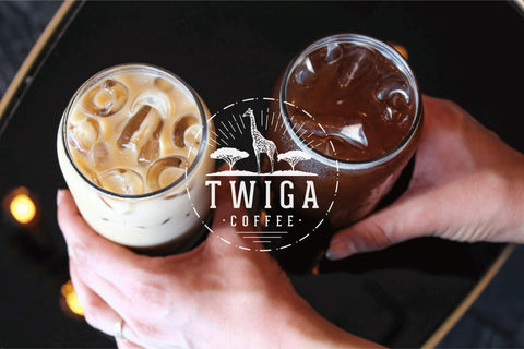 Two hands holding chilled coffees side by side, one pale with milk and ice and one dark and clear.