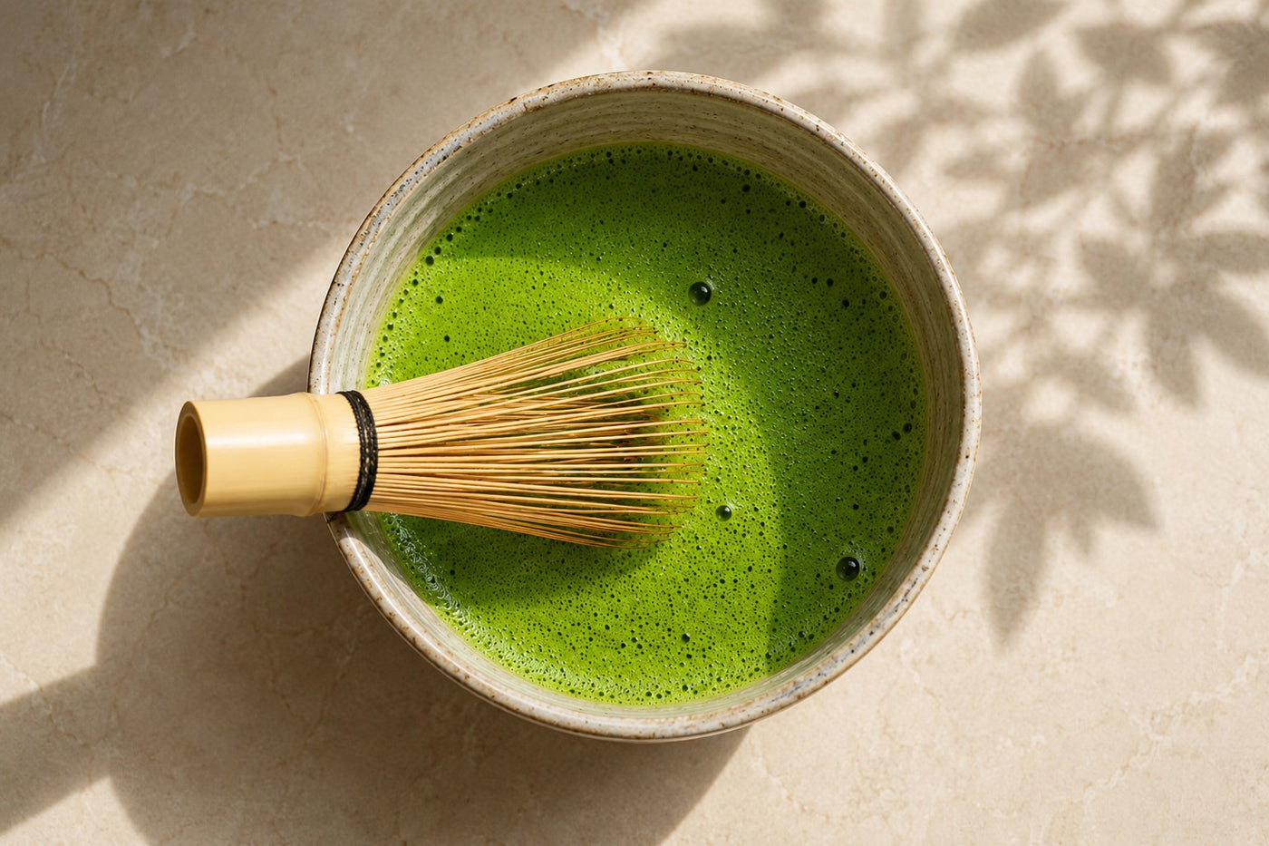 A bamboo whisk resting in a ceramic bowl of freshly whisked matcha, seen from above